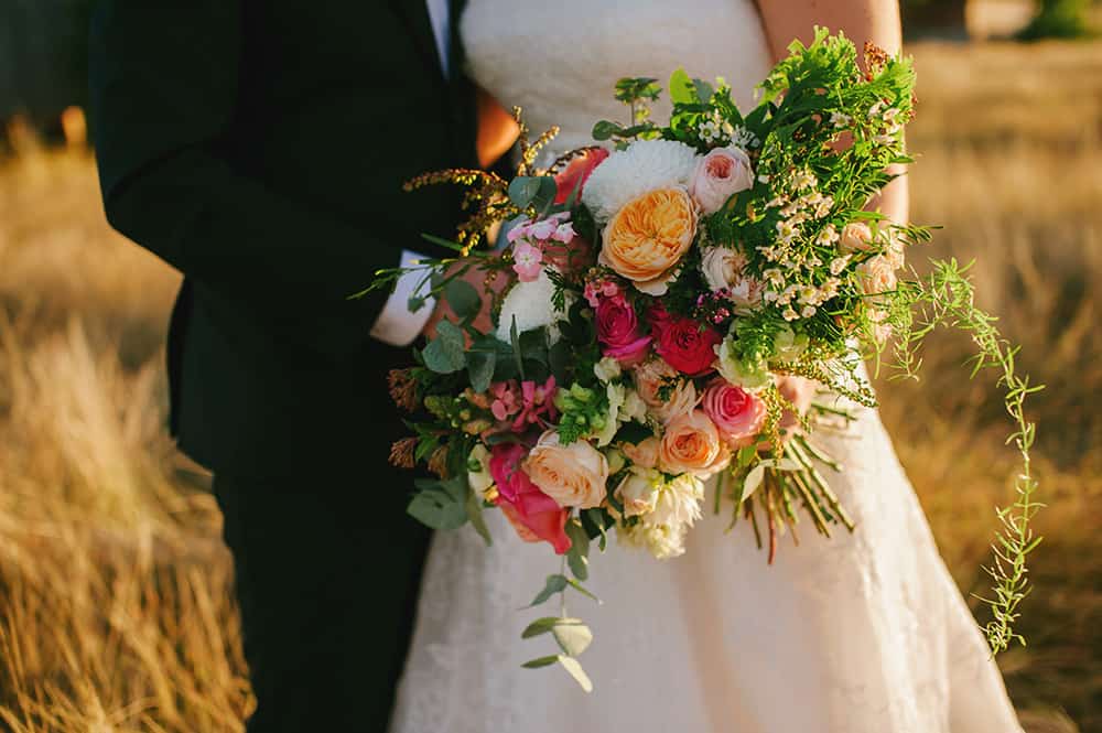 Cascading floral bouquet with Peach, coral and red roses and native ferns.