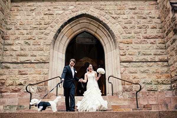 Bride and groom leaving church with their tuxedo dressed pup.